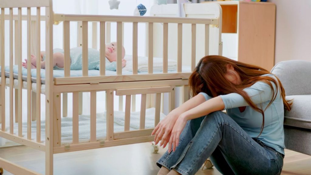 New mother feeling exhausted while holding her newborn at home, representing postpartum parenting stress.