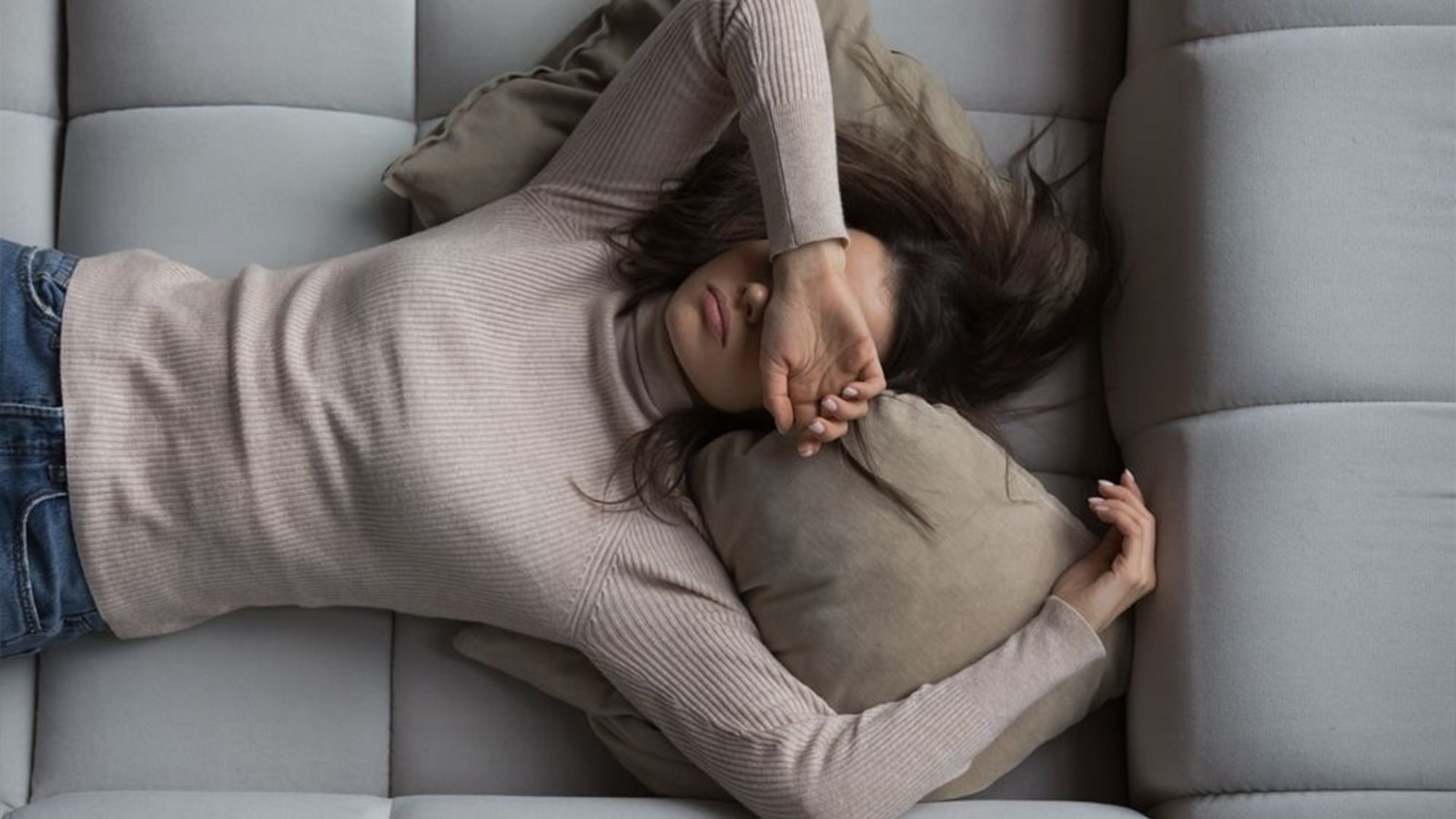 A tired woman lying on a couch with her arm covering her eyes, appearing emotionally and physically exhausted.